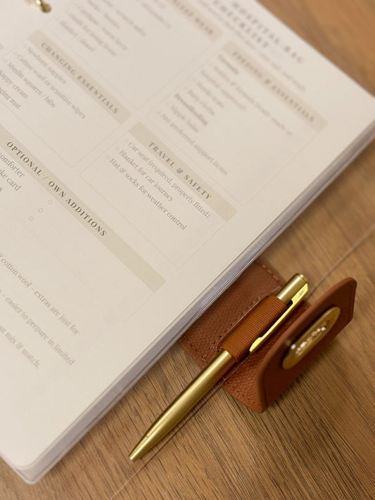 Open pregnancy journal with planning pages visible and a pen attached, placed on a wooden desk.