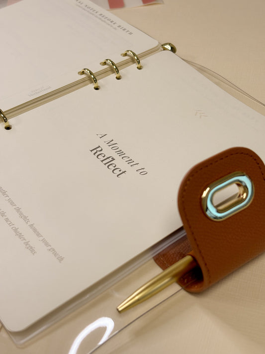 Open pregnancy journal showing a reflection page with a pen attached, inside a clear ring binder.